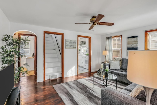 living room with arched walkways, visible vents, stairway, a ceiling fan, and wood finished floors