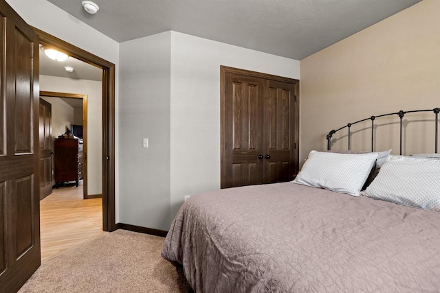 bedroom with a closet, light colored carpet, and baseboards