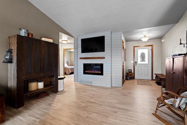 living room with lofted ceiling, light wood-style floors, visible vents, and a large fireplace