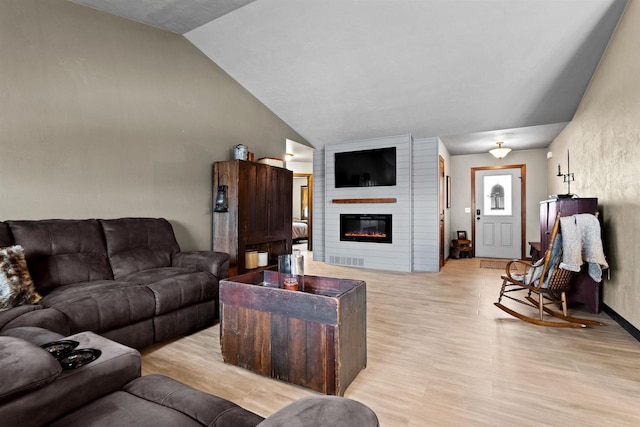 living area featuring light wood-type flooring, lofted ceiling, and a fireplace