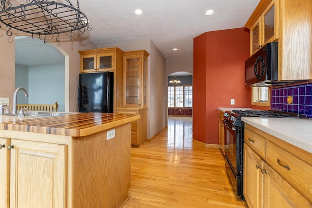 kitchen with arched walkways, light wood finished floors, butcher block counters, a sink, and black appliances