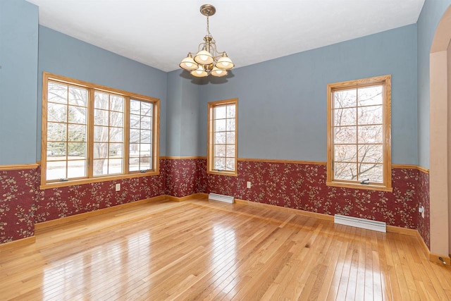 spare room with a notable chandelier, a baseboard heating unit, wainscoting, hardwood / wood-style floors, and wallpapered walls