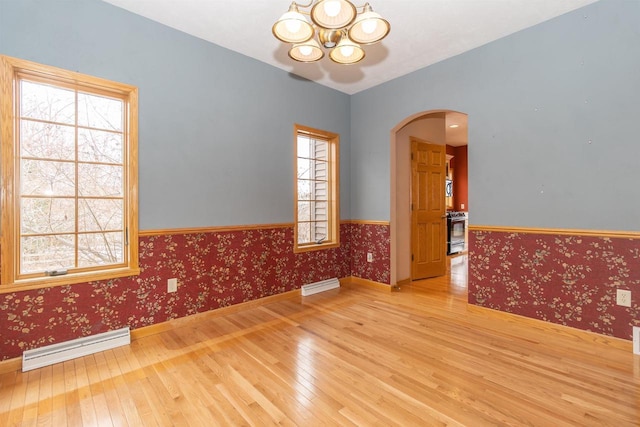 unfurnished room featuring wallpapered walls, arched walkways, wainscoting, hardwood / wood-style floors, and a baseboard heating unit