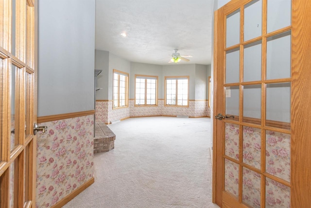 empty room featuring wallpapered walls, wainscoting, ceiling fan, a textured ceiling, and carpet floors