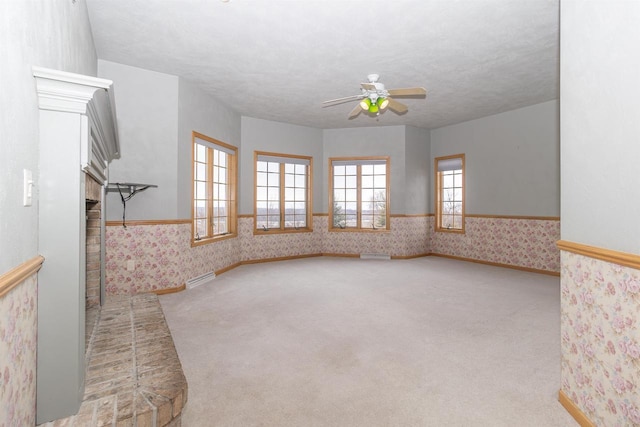 unfurnished room featuring a textured ceiling, a ceiling fan, baseboards, carpet, and wallpapered walls