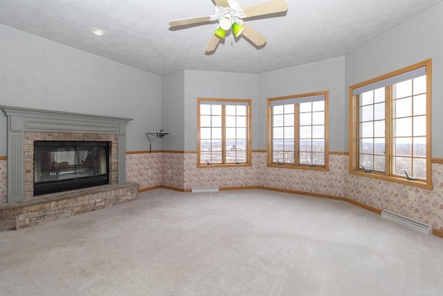 unfurnished living room with carpet floors, a fireplace, baseboard heating, baseboards, and wallpapered walls