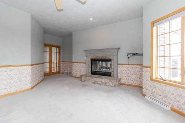 unfurnished living room featuring a healthy amount of sunlight, wallpapered walls, a brick fireplace, and a baseboard heating unit