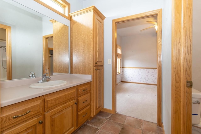 bathroom with wallpapered walls, baseboards, wainscoting, toilet, and vanity