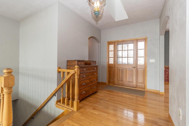 foyer featuring arched walkways, light wood-style flooring, baseboards, and a skylight