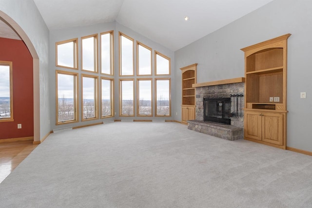 unfurnished living room featuring arched walkways, high vaulted ceiling, light colored carpet, a fireplace, and baseboards