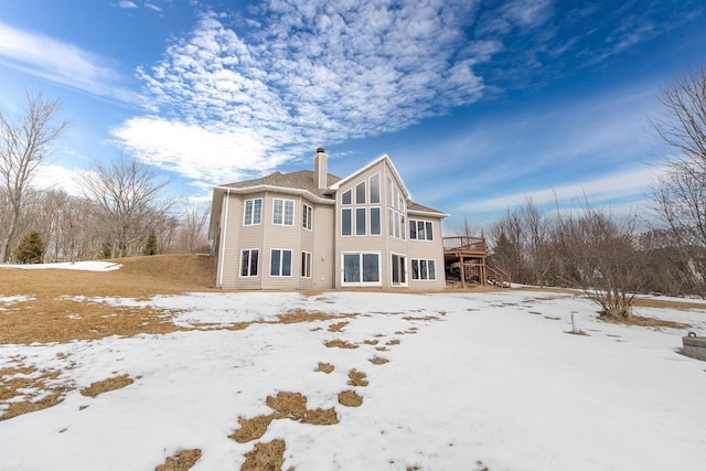 snow covered house with a deck, stairway, and a chimney