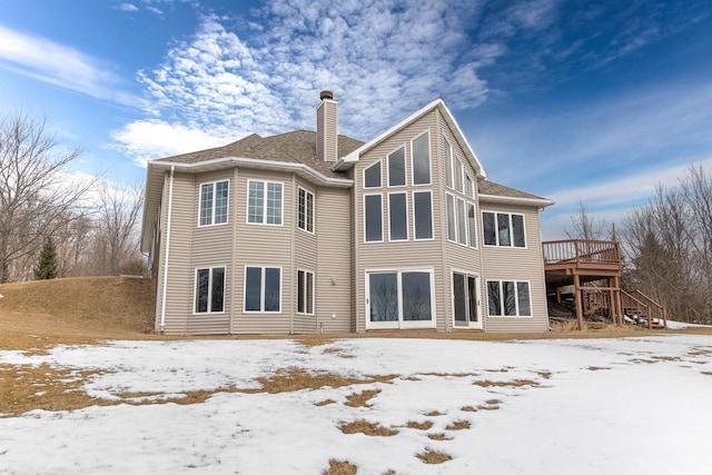 snow covered house with a deck, a chimney, and stairs