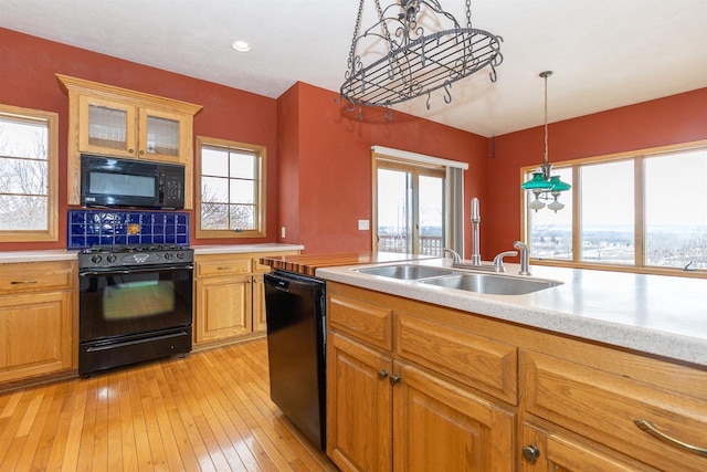 kitchen with light wood finished floors, light countertops, hanging light fixtures, glass insert cabinets, and black appliances