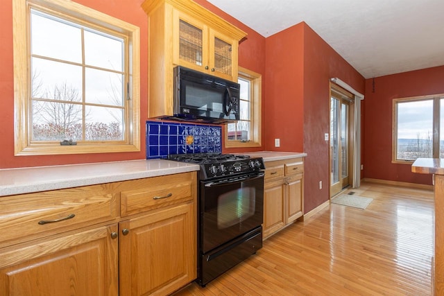 kitchen featuring light wood-style flooring, baseboards, light countertops, backsplash, and black appliances