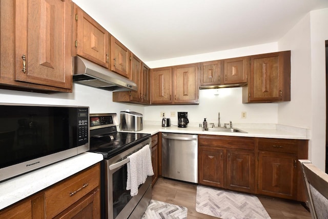 kitchen featuring brown cabinetry, appliances with stainless steel finishes, light countertops, under cabinet range hood, and a sink