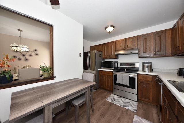 kitchen featuring decorative light fixtures, stainless steel appliances, light countertops, wood finished floors, and under cabinet range hood