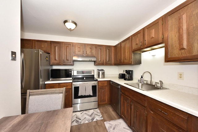 kitchen with light wood-style floors, appliances with stainless steel finishes, light countertops, under cabinet range hood, and a sink