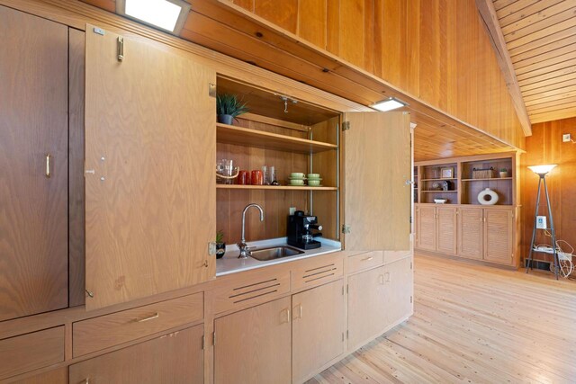 bar with lofted ceiling, wood ceiling, light wood-type flooring, wood walls, and a sink