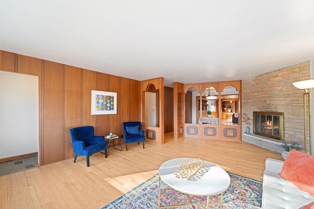 living area with wood walls, a stone fireplace, and wood finished floors