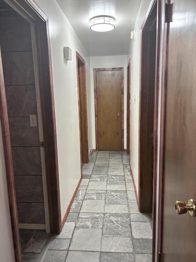 corridor featuring stone tile flooring and baseboards