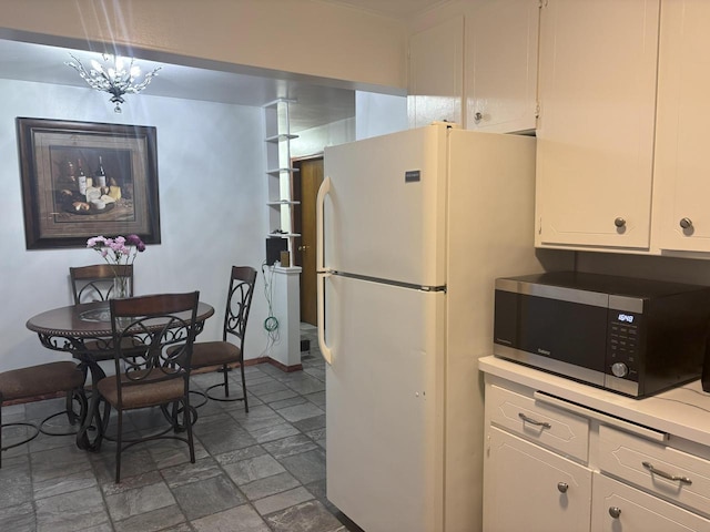 kitchen with light countertops, stainless steel microwave, freestanding refrigerator, stone finish floor, and white cabinetry