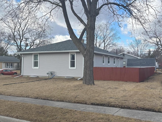 view of side of property featuring a shingled roof, a lawn, and fence