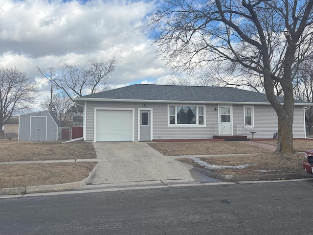 ranch-style house with an outbuilding, an attached garage, concrete driveway, roof with shingles, and a storage unit