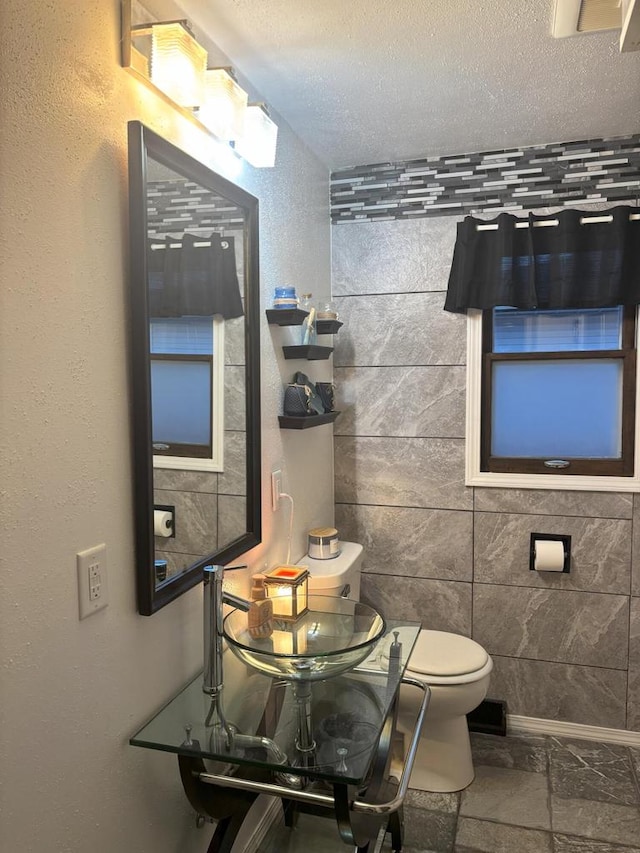 bathroom with a textured ceiling, stone tile flooring, a sink, and toilet