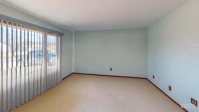 empty room with a textured ceiling, baseboards, and light colored carpet