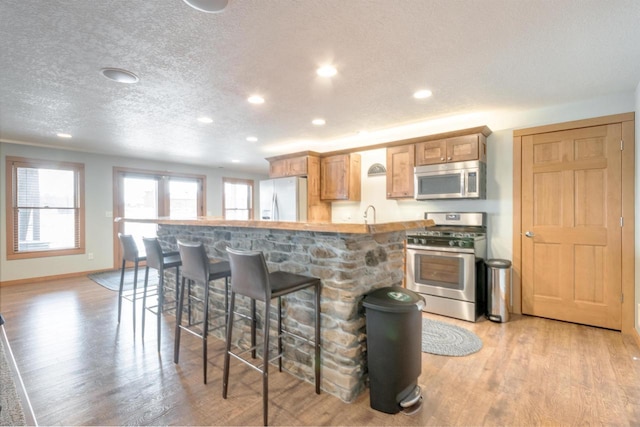 N8111 Castaway Dr, New Lisbon, WI 53950 - kitchen featuring light wood finished floors, baseboards, appliances with stainless steel finishes, a kitchen breakfast bar, and a textured ceiling