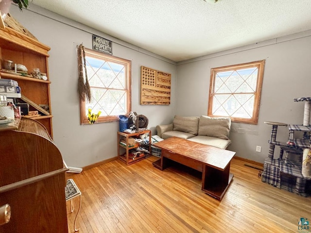 living area featuring light wood-type flooring, baseboards, and a textured ceiling