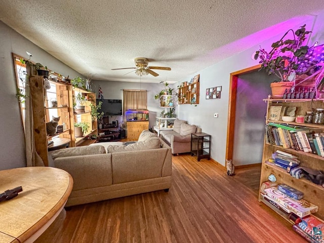 living area featuring a ceiling fan, a textured ceiling, baseboards, and wood finished floors