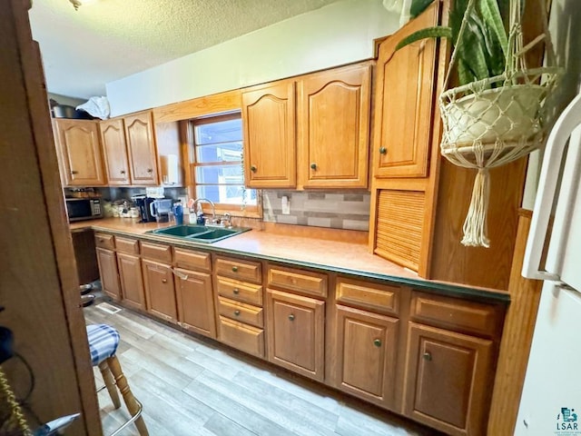 kitchen with light wood finished floors, freestanding refrigerator, a sink, a textured ceiling, and backsplash