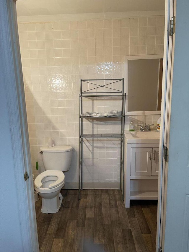 half bath with toilet, vanity, wood finished floors, and tile walls