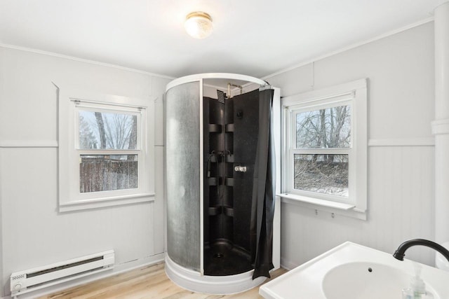 full bathroom featuring a stall shower, a baseboard radiator, wood finished floors, crown molding, and a sink