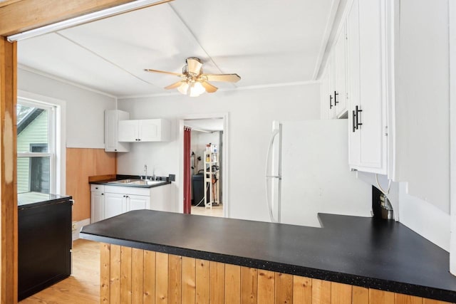 kitchen with white cabinets, dark countertops, freestanding refrigerator, a peninsula, and a sink