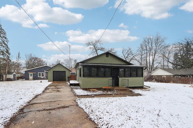 bungalow-style house with a sunroom, a detached garage, concrete driveway, and an outbuilding