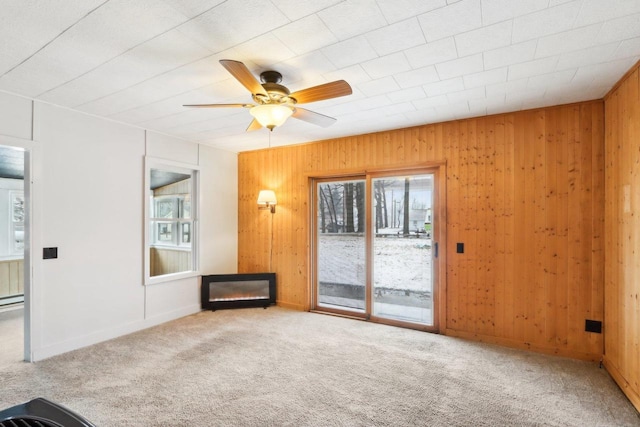 interior space with ceiling fan, wood walls, a warm lit fireplace, and carpet