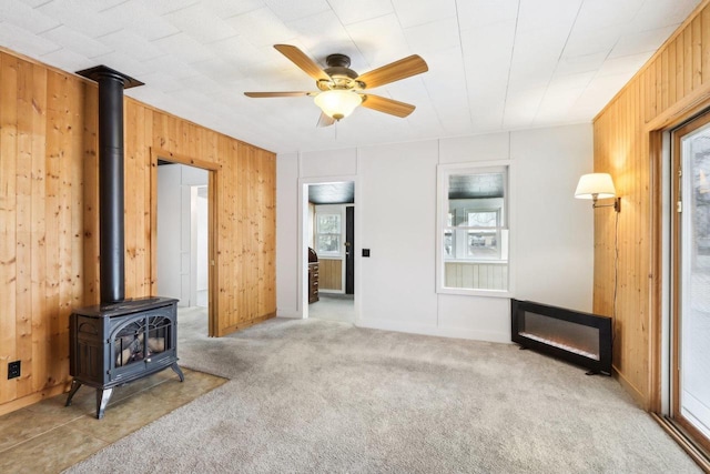 living area with a wood stove, light colored carpet, wood walls, and ceiling fan