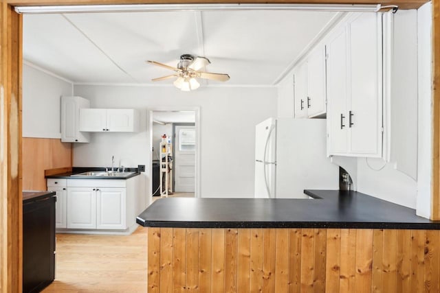 kitchen with dark countertops, freestanding refrigerator, a peninsula, white cabinetry, and a sink