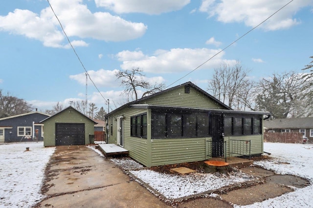 exterior space featuring a garage, concrete driveway, an outdoor structure, and a sunroom