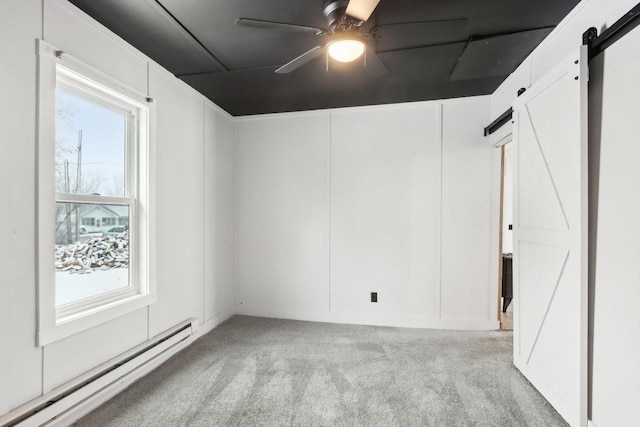 empty room featuring ceiling fan, a barn door, baseboard heating, and carpet flooring