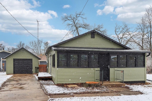 bungalow with a sunroom, concrete driveway, a detached garage, and an outdoor structure