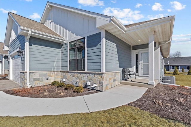 exterior space featuring covered porch, stone siding, board and batten siding, and an attached garage