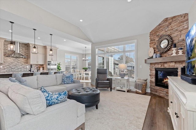 living area with lofted ceiling, dark wood-type flooring, a stone fireplace, a chandelier, and recessed lighting