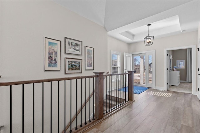 corridor with baseboards, a raised ceiling, wood finished floors, an inviting chandelier, and an upstairs landing