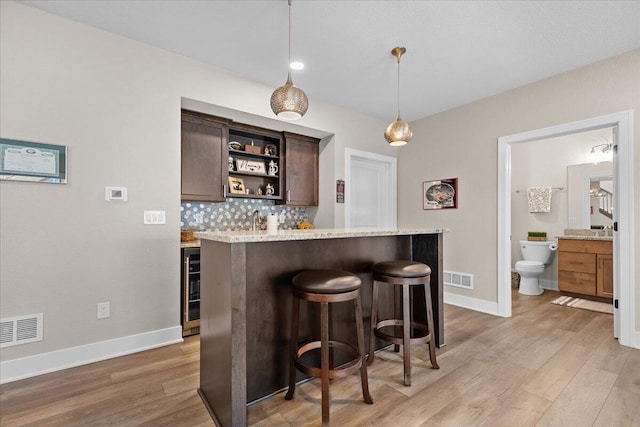 bar with light wood finished floors, tasteful backsplash, visible vents, and wet bar