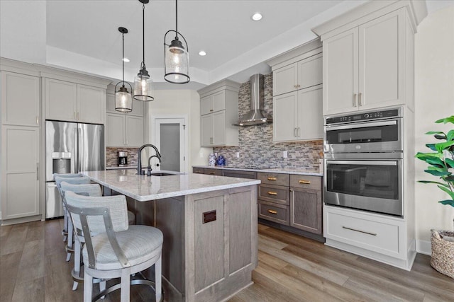 kitchen featuring decorative backsplash, appliances with stainless steel finishes, a sink, wall chimney range hood, and wood finished floors