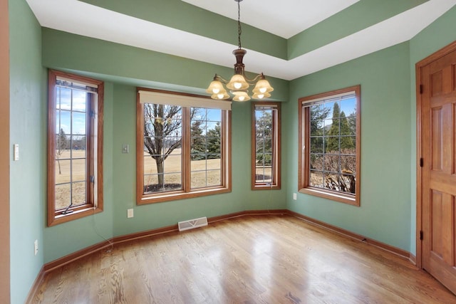 unfurnished dining area with visible vents, baseboards, a raised ceiling, wood finished floors, and a notable chandelier