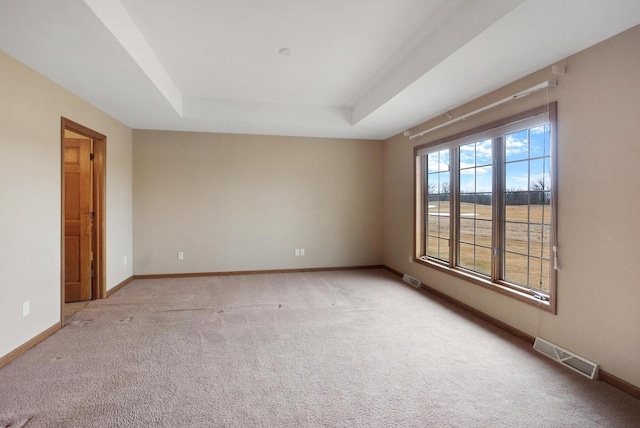 spare room with light carpet, visible vents, a tray ceiling, and baseboards